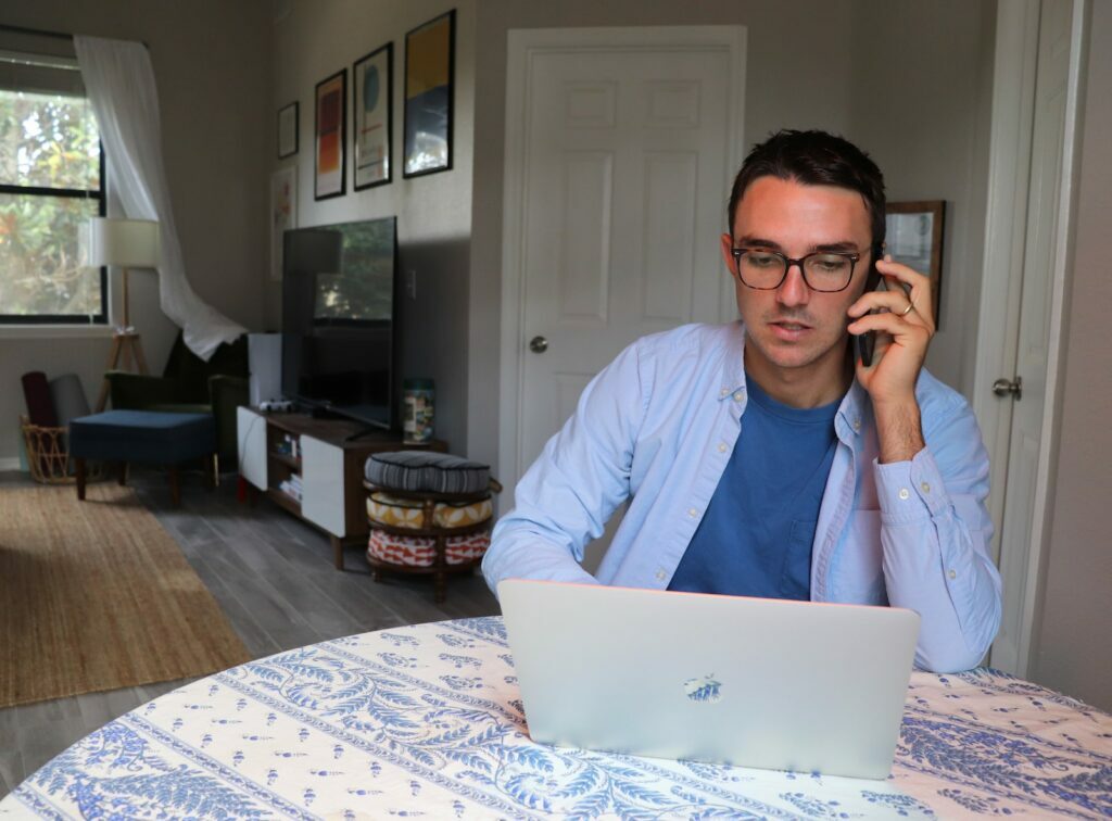 Home Office Involves man in white dress shirt wearing eyeglasses sitting by the table using macbook