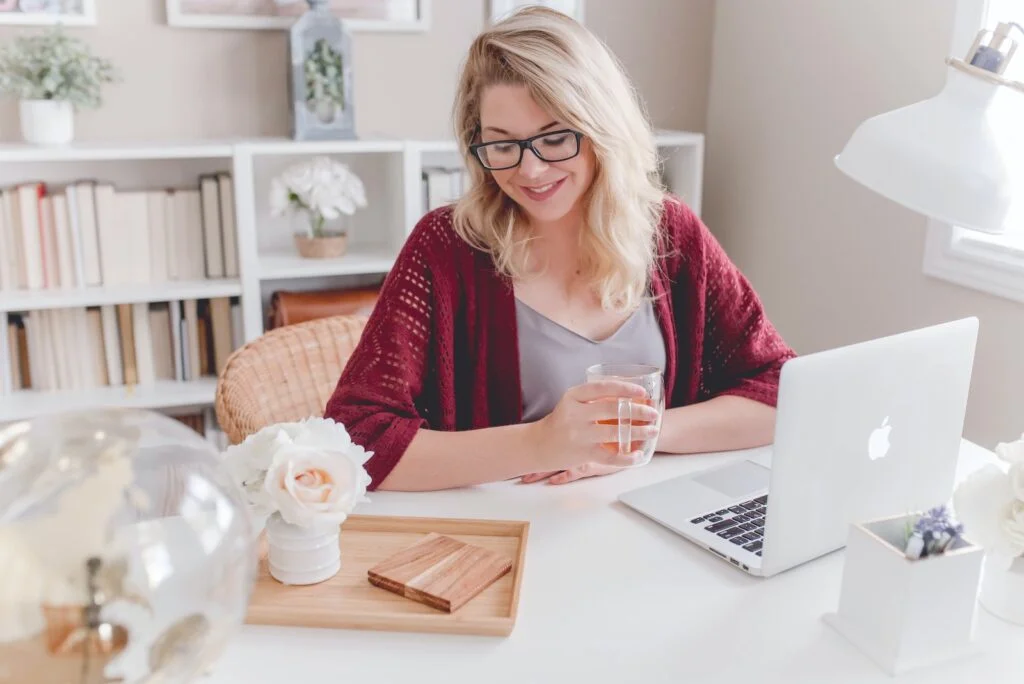 Inmetrics woman smiling holding glass mug sitting beside table with MacBook