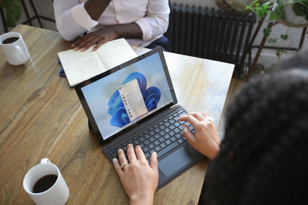 22 Vagas de Emprego na Conexão Talento Overhead view of two people at a table working with a Microsoft laptop and notebook